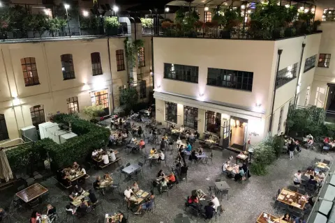 Serata vivace al birrificio La Piazza, con tavoli all'aperto pieni di gente che gode della buona compagnia e delle birre artigianali.