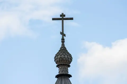 Drewniany krzyż na kopule cerkwi, symbol gruzińskiej religii prawosławnej, na tle błękitnego nieba z chmurami.