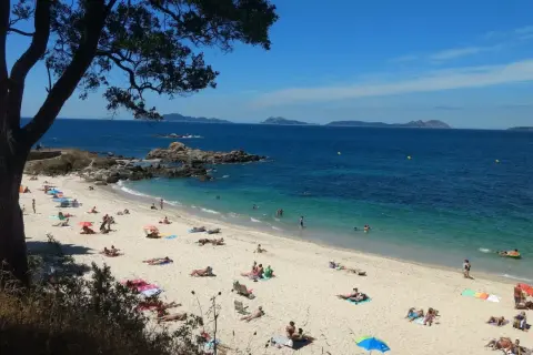 Gente disfrutando del sol y el mar en la **praia do tombo do gato**. Aguas cristalinas y arena dorada bajo un cielo azul.