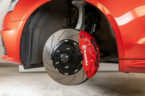 Gros plan sur un étrier de frein Brembo rouge vif sur une voiture de sport. Le disque de frein rainuré est visible. Idéal pour connaître le tarif changement étrier de frein.