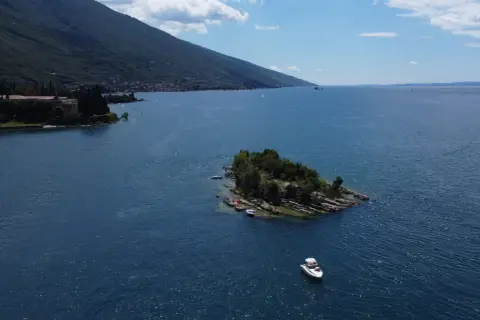 Un'isola verdeggiante nel Lago di Garda, con piccole imbarcazioni ormeggiate e una barca a motore che naviga nelle acque azzurre.