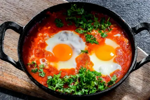 Herzhaftes Shakshuka-Rezept: Eier in würziger Tomatensoße, garniert mit frischer Petersilie, serviert in einer Gusseisenpfanne.