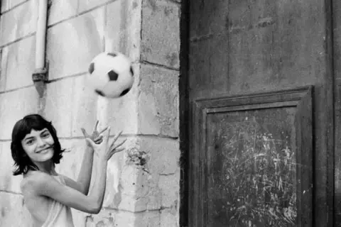 Letizia Battaglia giovane gioca con un pallone, un'immagine che cattura la spensieratezza dell'infanzia.