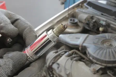 Zużyta świeca zapłonowa, która może być przyczyną wypadania zapłonu, w dłoni mechanika na tle silnika samochodu.