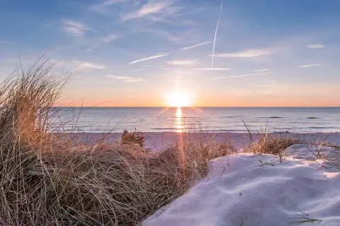 Sonnenuntergang am Strand, ein perfekter Urlaub in Deutschland. Dünen mit Gräsern und Sand, das Meer glitzert.