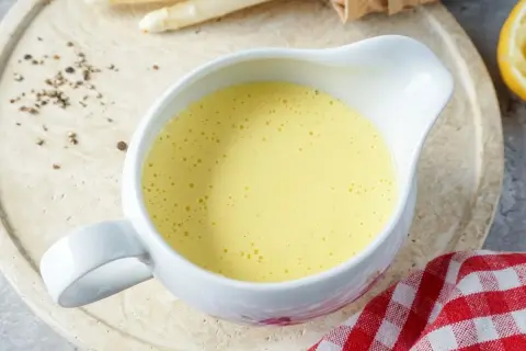 Cremige Sauce Hollandaise in einer Sauciere, daneben Spargel und Zitronenspalte. Perfekt für ein Frühlingsgericht.