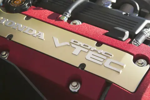 Złota pokrywa zaworów z napisem HONDA VTEC w czerwonej obudowie silnika.
