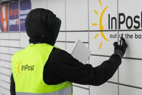 Pracownik w kamizelce InPost z paczką przy paczkomacie. Czy muszę naklejać etykietę InPost? Nie, wystarczy kod nadany przez system.