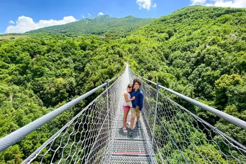 Bambini su un percorso ponte tibetano, circondati da una lussureggiante foresta verde sotto un cielo azzurro.