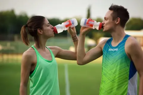 Zwei Athleten trinken nach dem Sport. Sie halten ihre Wasserflaschen und erfrischen sich auf dem Feld.