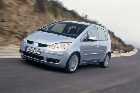 Srebrny Mitsubishi Colt VI pokonuje zakręt na krętej drodze, otoczony przez wzgórza.