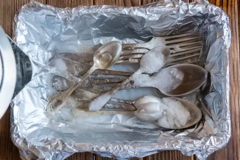 Jak wyczyścić poczerniałe sztućce? Woda z czajnika zalewa srebrne łyżki i widelce w folii aluminiowej, tworząc pianę.