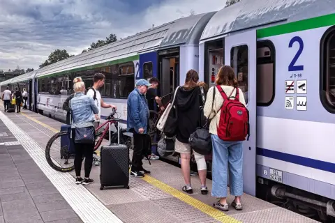 Ludzie wsiadają do pociągu PKP. Wśród nich starszy pan, młodzi ludzie z rowerem i bagażami. Może właśnie korzystają z **pkp zniżki dla niepełnosprawnych stopień lekki**?