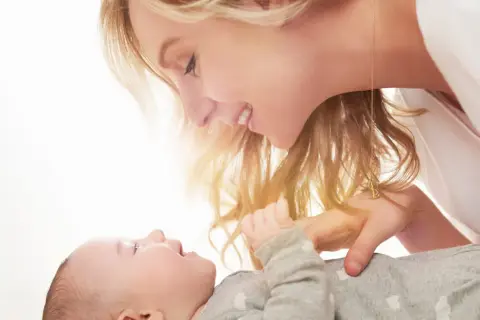 Uśmiechnięta mama pochyla się nad dzieckiem, które ma czkawkę u noworodka.