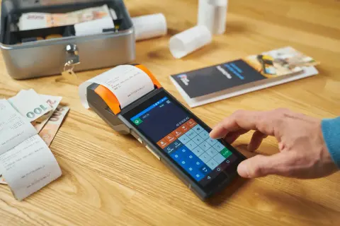 Działalność nierejestrowana a kasa fiskalna: na drewnianym blacie leży terminal płatniczy, banknoty i paragon.