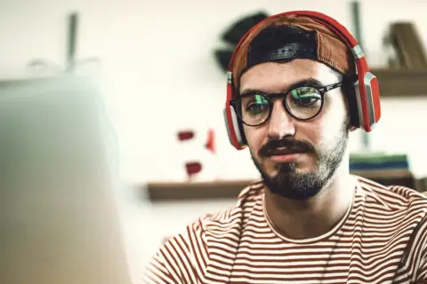 Junger Mann mit Kopfhörern und Brille lernt für seinen berufsbegleitenden Master in Stuttgart.
