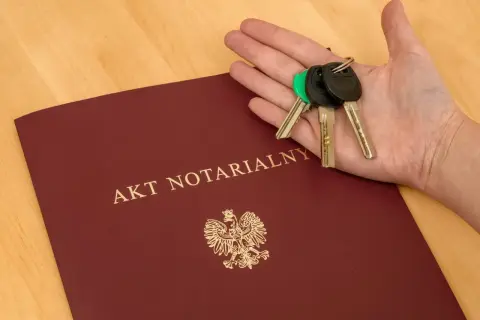 Akt notarialny i klucze w dłoni. Dokument z godłem Polski, symbolizuje finalizację transakcji, jak zakup mieszkania. To ważny wpis do repertorium.