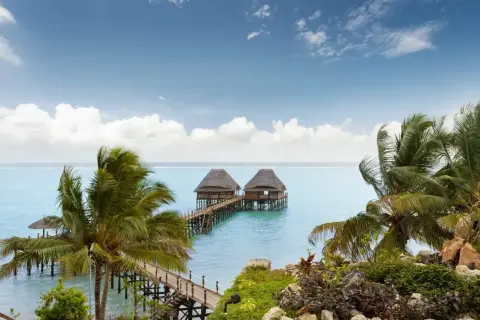 Dwa domki na wodzie na Zanzibarze, otoczone palmami. Nawet podczas pory deszczowej Zanzibar zachwyca pięknem.