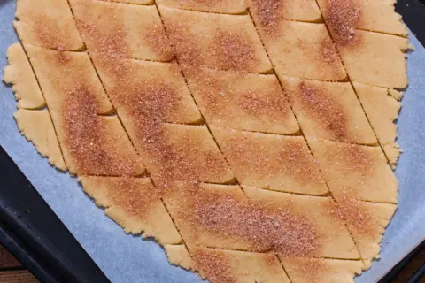 Surowe ciasto na ciasteczka pokrojone w romby, posypane cukrem z cynamonem.