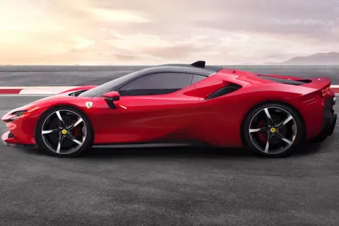 Czerwone Ferrari SF90 na torze wyścigowym, z czarnym dachem i felgami. Słońce zachodzi za górami.