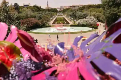 Flores vibrantes en primer plano, con el parque grande Zaragoza florece al fondo, destacando una fuente y senderos verdes.