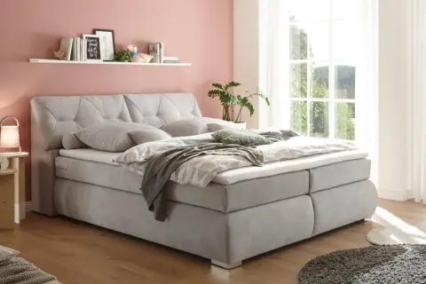 Einladendes, graues Boxspringbett mit gestepptem Kopfteil, das Ruhe und Harmonie ausstrahlt – perfekt für ein Feng Shui Bett.