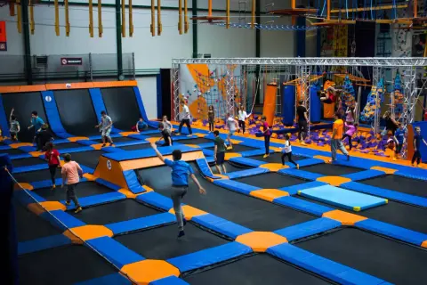 Dzieci skaczą na trampolinach w największym parku trampolin w Polsce. W tle widać ściankę wspinaczkową i tor przeszkód.
