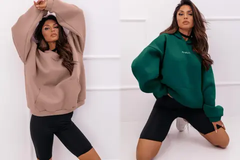 Dwie kobiety w beżowych i zielonych bluzach oversize, które wyglądają na za duże ubrania, w połączeniu z czarnymi szortami.