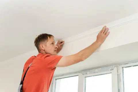 Hombre instalando moldura de escayola en el techo. Aprende como hacer escayola para techo y embellece tu hogar.