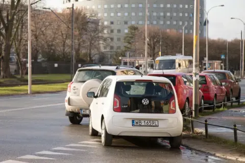 Biały Volkswagen i inne samochody stojące na ulicy, typowe parkowanie w Wiedniu.