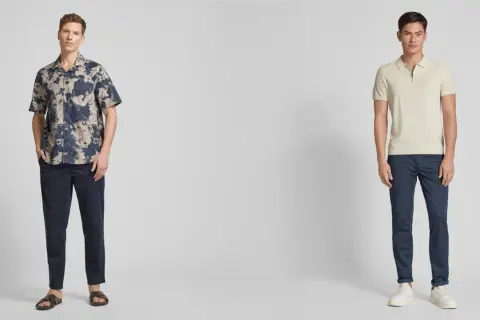Zwei Männer präsentieren lässige Outfits. Der linke trägt ein gemustertes Hemd zu dunkelblauen Chinos. Der rechte kombiniert ein helles Poloshirt mit denselben blauen Chinos.