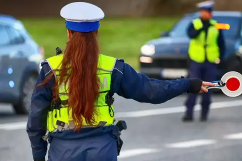 Policjantka zatrzymuje ruch, by uniknąć mandatu 24 punkty karne. Inny funkcjonariusz kieruje ruchem.