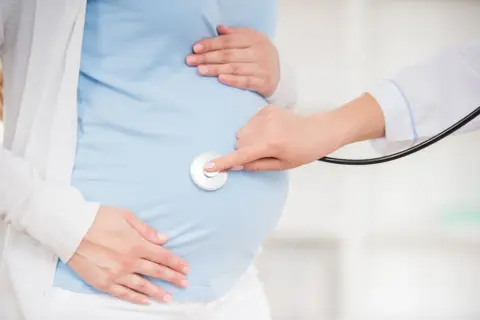 Lekarz osłuchuje brzuch ciężarnej, sprawdzając, czy nie ma ułożenia poprzecznego, które mogłoby wymagać cesarki.
