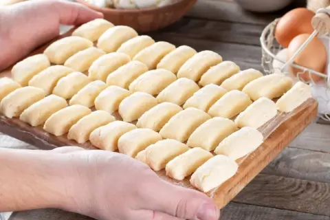 Ania gotuje pierogi leniwe. Na desce ułożone są rzędy gotowych do gotowania pierogów leniwych.