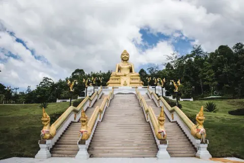 Goldene Buddha-Statue über einer langen Treppe mit Naga-Schlangen-Geländern in Nakhon Si Thammarat.