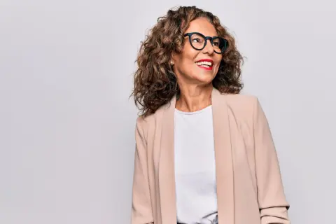 Donna sorridente con occhiali e blazer beige, un esempio di come vestirsi a 50 anni con stile.