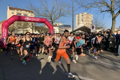 Départ d'une course à Bourg-en-Bresse sous un ciel bleu. Des coureurs s'élancent sous une arche rose.