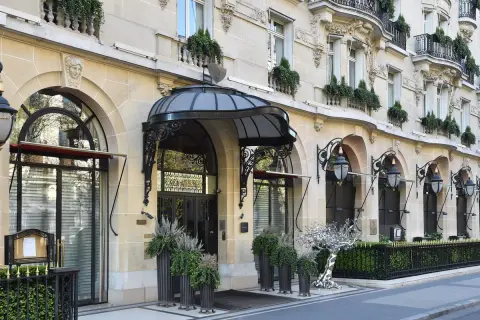 L'elegante ingresso di un edificio parigino, forse sede di Alain Ducasse a Parigi, con lampioni classici e piante verdi.
