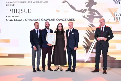 Cztery osoby w garniturach i sukience stoją na scenie, odbierając nagrodę.