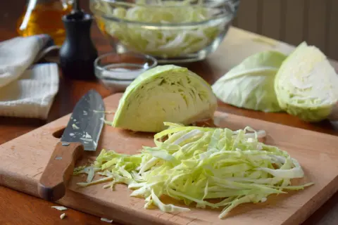 Frisch geschnittener Weißkohl liegt auf einem Holzbrett, bereit für ein Sauerkraut Rezept. Daneben ein Messer und Schüssel mit Kohl.