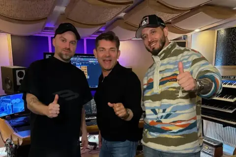 Mariusz Kalaga, jedna z gwiazd, w studiu nagraniowym z przyjaciółmi. Wszyscy pokazują kciuki w górę, gotowi do tworzenia muzyki.