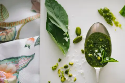 Łyżka pełna aromatycznego pesto z rukoli, obok pistacje i listki bazylii.