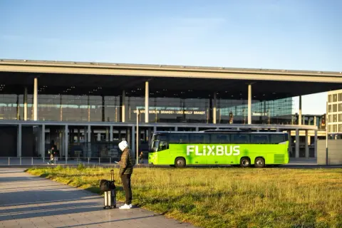 Mann mit Koffer wartet auf den Flixbus am Flughafen Berlin Brandenburg. Eine Direktverbindung Dresden Berlin Flughafen ist hier möglich.