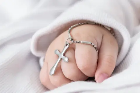 Dziecięca rączka z krzyżykiem na łańcuszku, symbol błogosławieństwa podczas chrztu dziecka.
