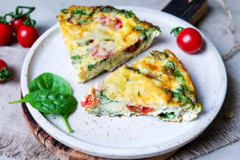 Zwei Stücke einer herzhaften Frittata mit Spinat und Tomaten auf einem Teller, garniert mit frischen Spinatblättern und Kirschtomaten. Ein köstliches Frittata Rezept.