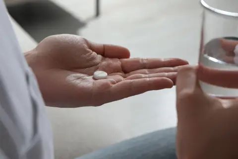 En hand håller en tablett, redo att sväljas med ett glas vatten. Detta kan vara en del av förklaringen till hur funkar antidepressiva.