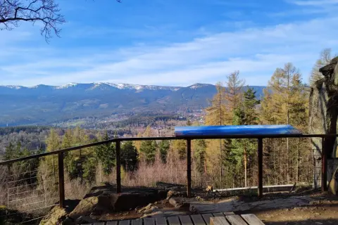 Widok z punktu widokowego na góry, las i miasteczko. Na pierwszym planie drewniany taras i balustrada. W oddali majaczy zakręt śmierci.