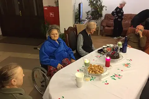 Wspólne świętowanie w domu seniora Zacisze. Przy stole tort, ciastka i świece.