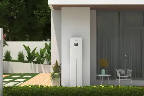 Biały magazyn energii 5 kW, idealny do zasilania domu. Obok nowoczesne drzwi, ogród i taras.