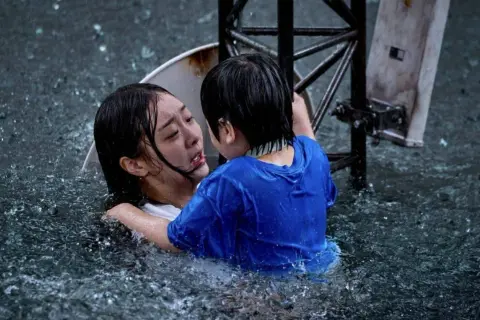 Dramatyczna scena z najlepszych filmów koreańskich: dziecko obejmuje tonącą kobietę w ulewnym deszczu.